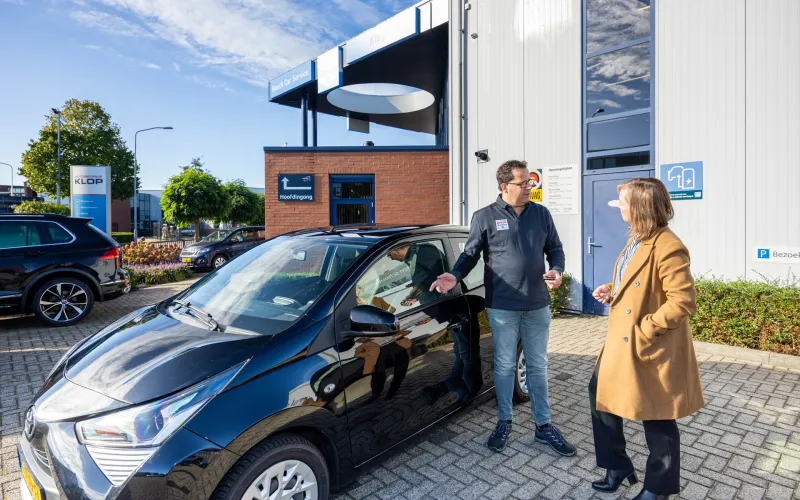 Vrouw en autoverkoper staan naast auto